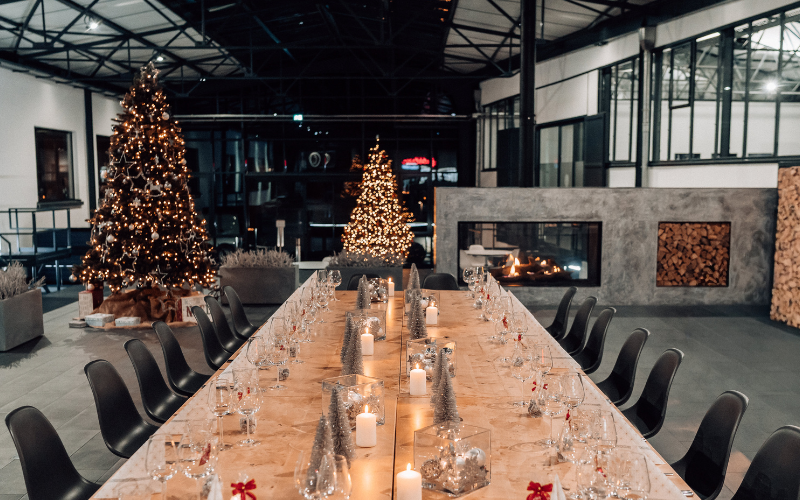 Weihnachtsfeier im Atrium bei Ebbtron Solingen: festlich gedeckte Tafel mit Kerzen und Weihnachtsbäumen in moderner Eventlocation für Firmenfeiern und Business Events.“